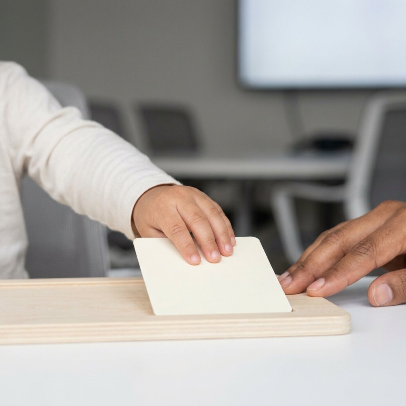 Extreme close-up of a small child's hands placing a plain picture card onto a board, an adult's fingertips steadying the edge.