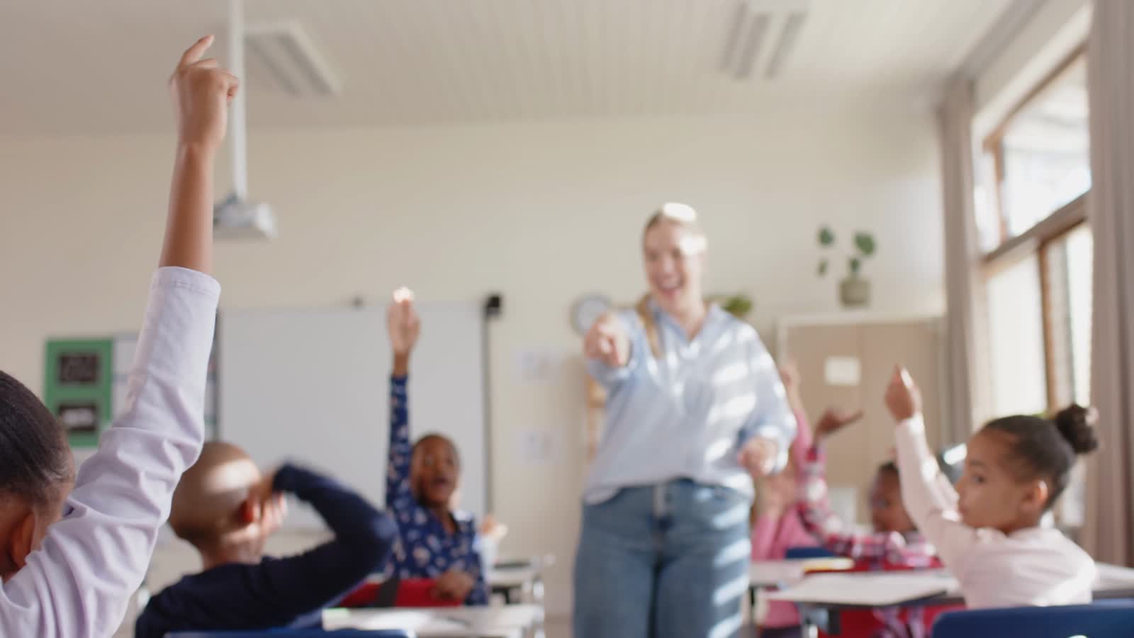 Students raising their hands in a classroom as a teacher calls on them