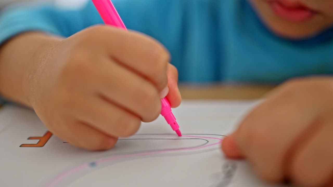 A close-up of a child tracing a dotted outline with a marker