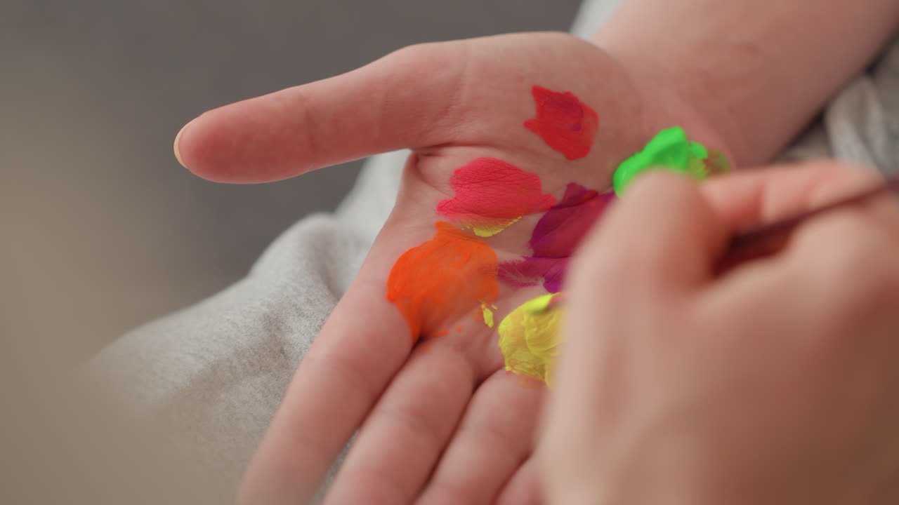 A close-up of a therapist painting colours onto a child's open palm during a sensory activity