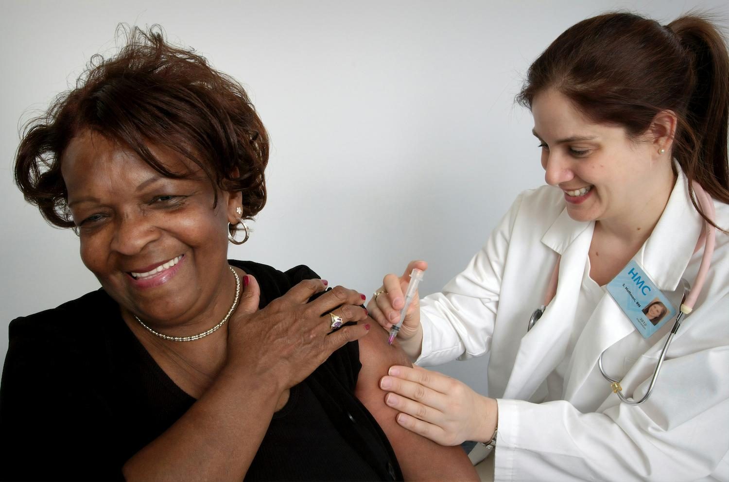 A nurse gives a smiling patient an injection in her upper arm