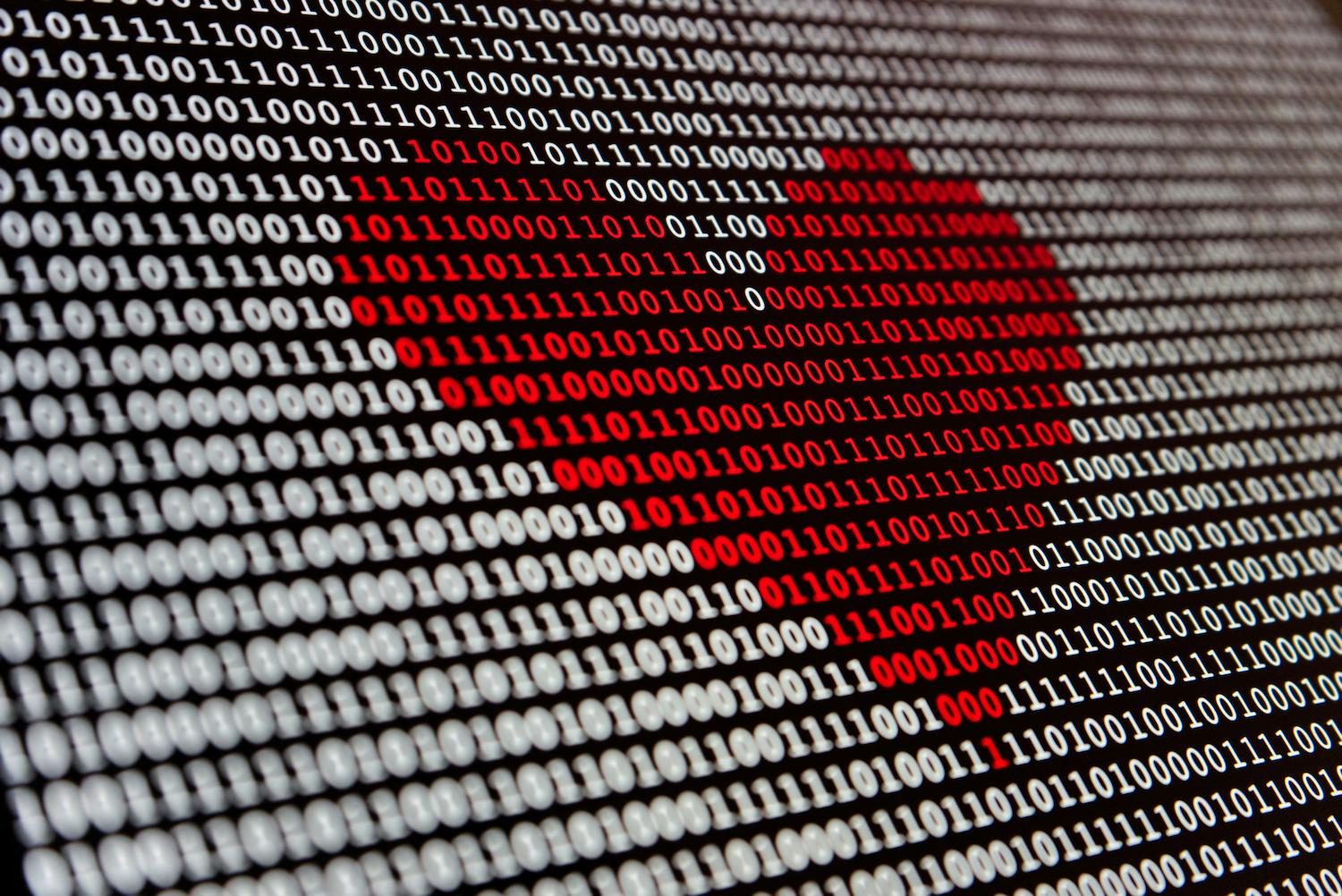 Rows of binary code on a screen, with a red heart shape formed in the digits